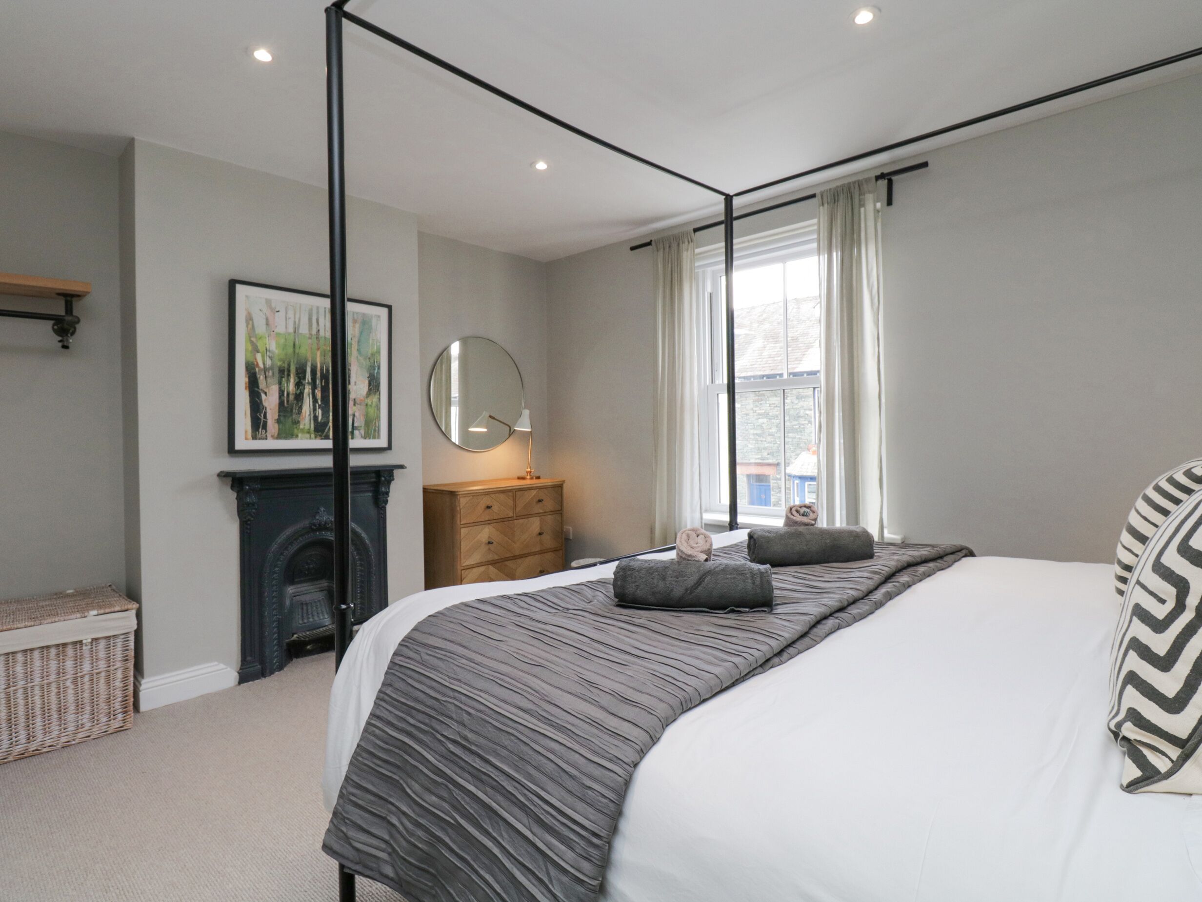 A bedroom with a large bed, a fireplace, a dresser, and a window with curtains.