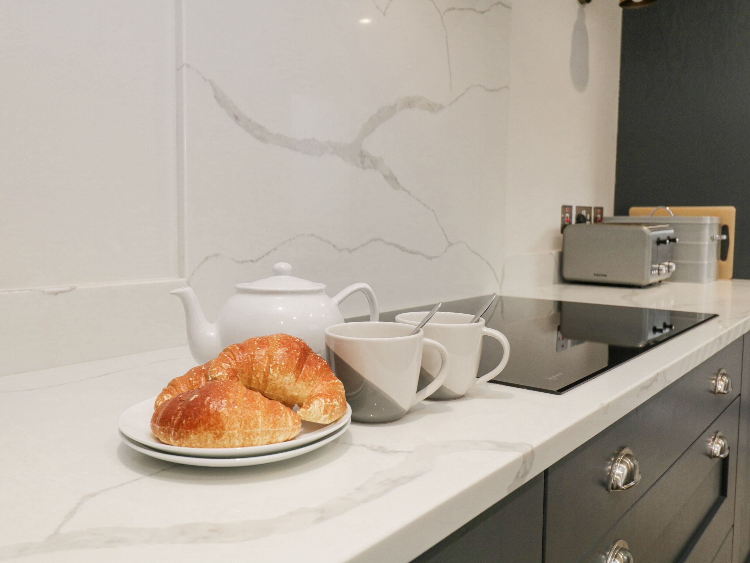 Une cuisine avec un plan de travail en marbre, une théière, deux tasses et un grille-pain.
