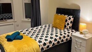 A bedroom with a bed, a bedside table, a window with curtains, and a nightstand with a lamp. - Central Location 2-bed Apartment in Maidstone (Maidstone)