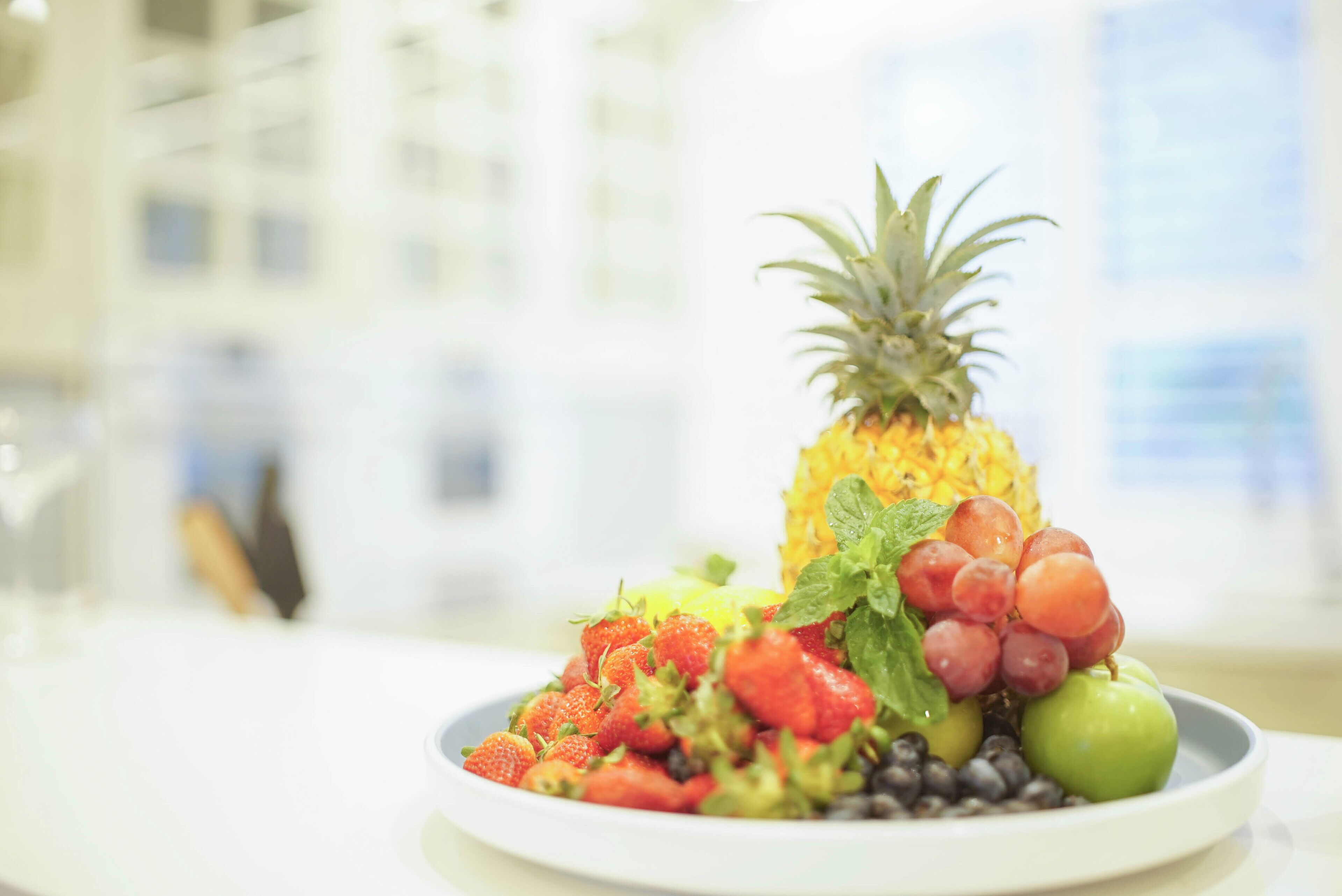 A plate of fresh fruits including strawberries, grapes, blueberries, a pineapple, and an apple.