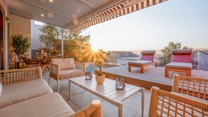 A sunlit outdoor patio with wicker furniture, a wooden deck, and a view of the sunset. - The Weinberg Urban Pods (Windhoek)
