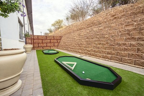 Un campo de mini golf con dos áreas de putting y un muro de ladrillo al fondo.