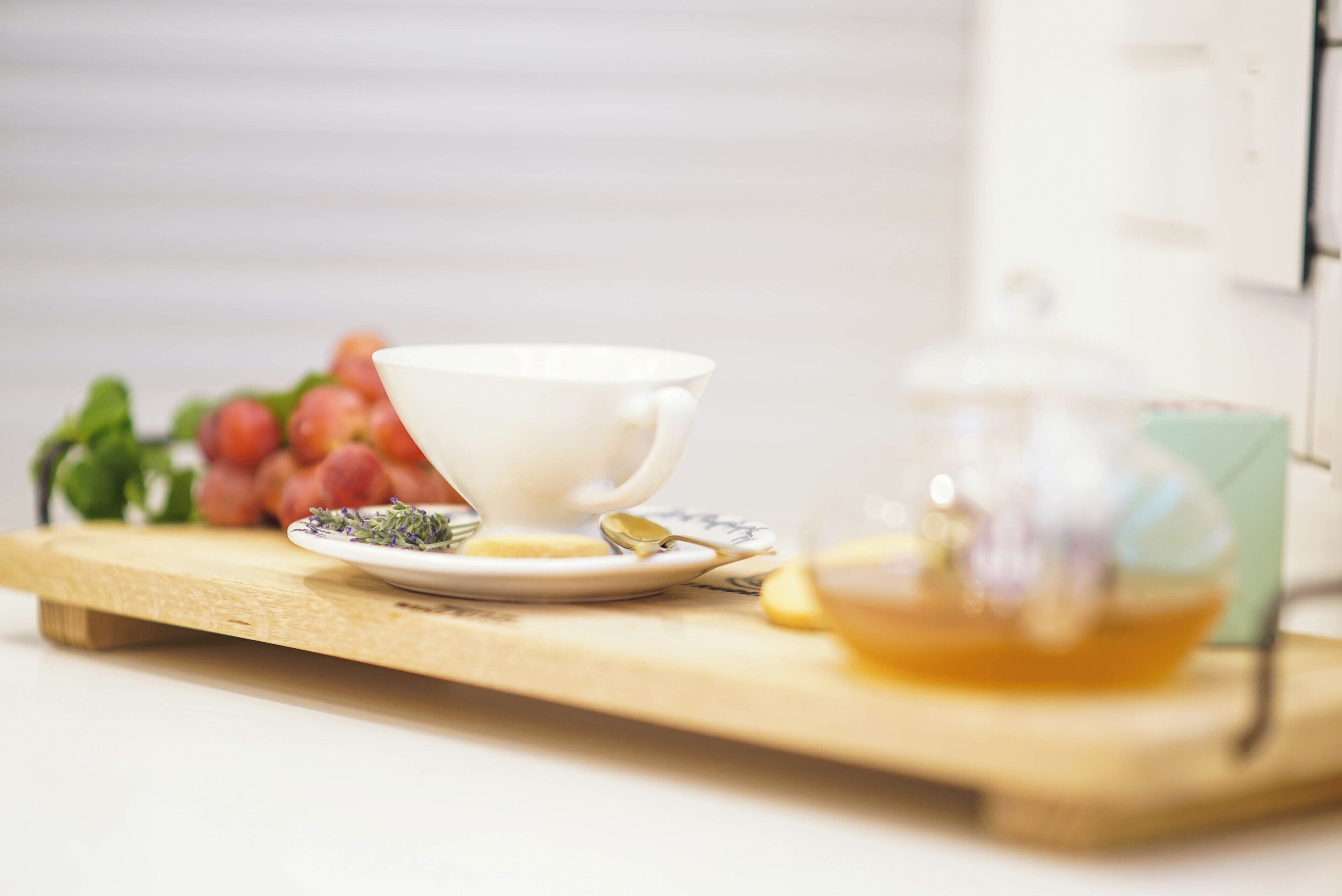 A white cup on a wooden tray with a teapot and a plate of tea leaves.