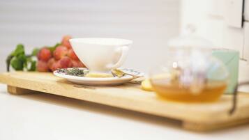 A white cup on a wooden tray with a teapot and a plate of tea leaves.
