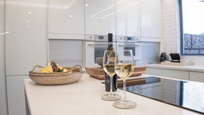 A modern kitchen with a glass counter, a wine bottle, and two wine glasses. - The Weinberg Urban Pods (Windhoek)