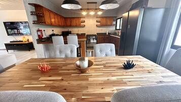 Une cuisine moderne avec des meubles en bois, une table à manger avec des chaises et des luminaires suspendus.
