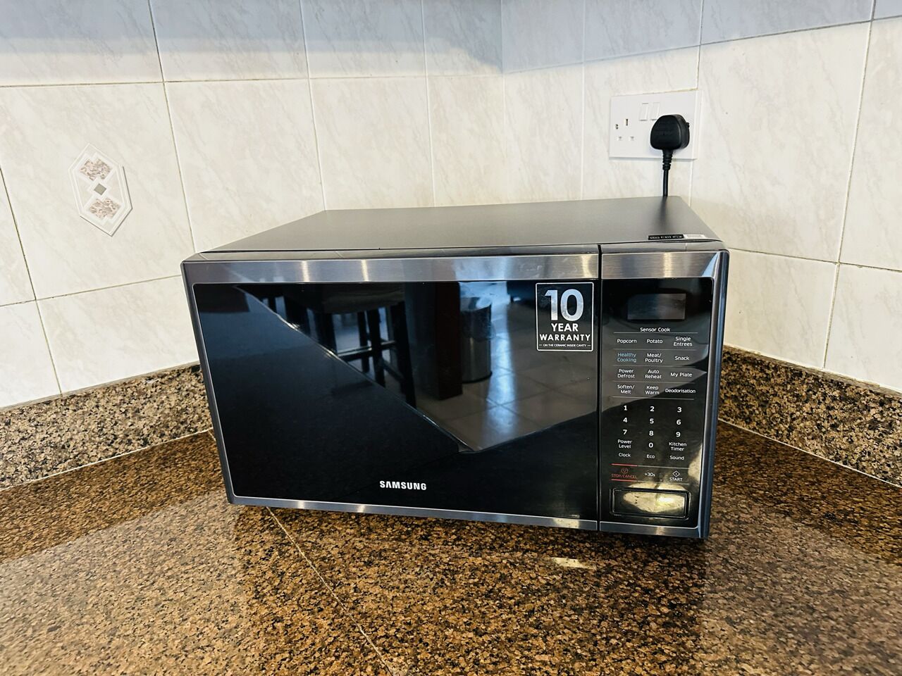 Un horno microondas Samsung con una garantía de 10 años, sobre una encimera de granito.