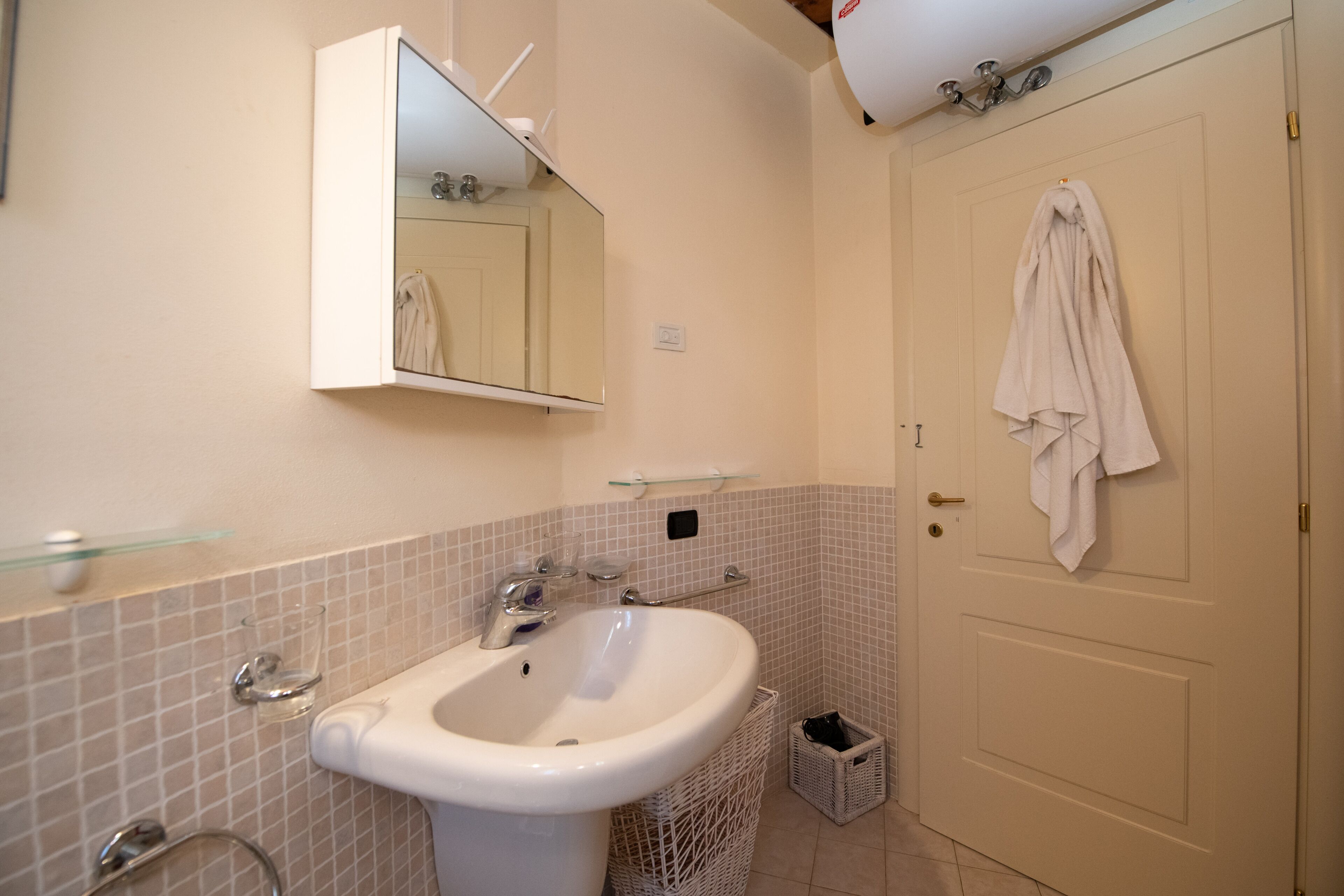 A bathroom with a sink, mirror, and towel hanging on the door.