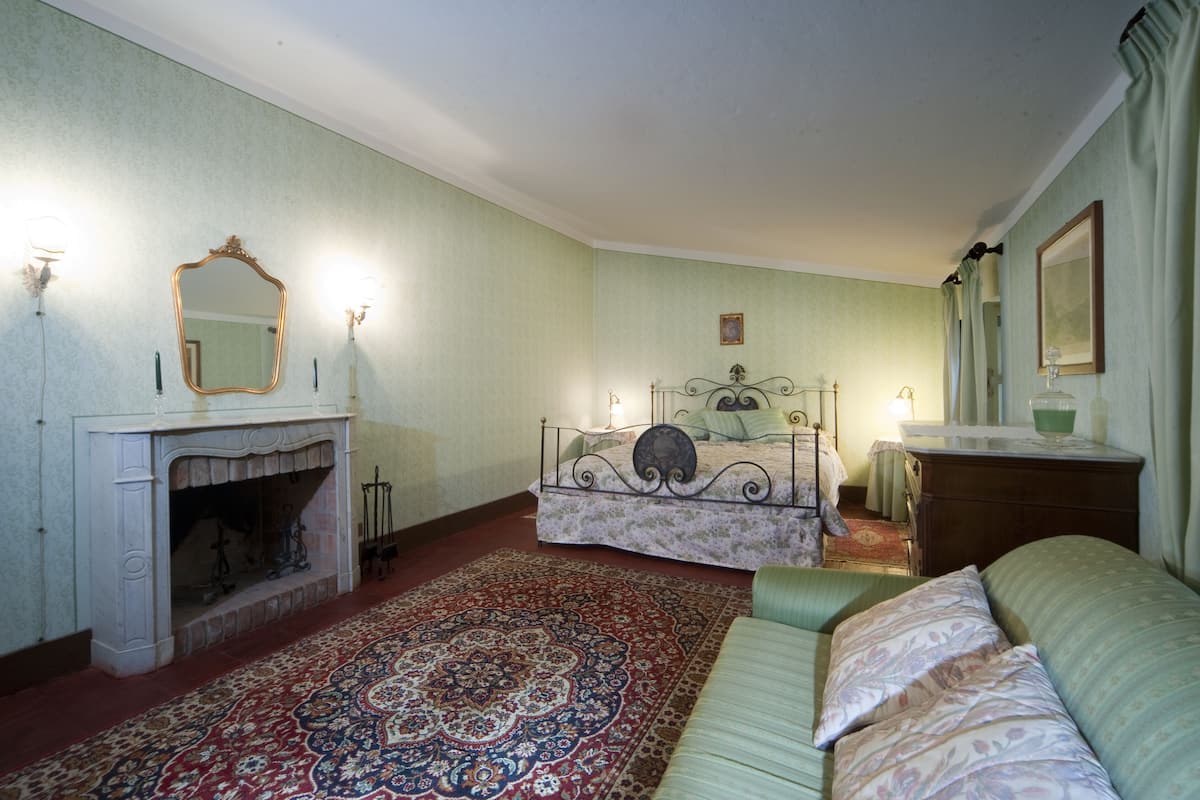 A room with a bed, a green sofa, a fireplace, and a mirror on the wall.