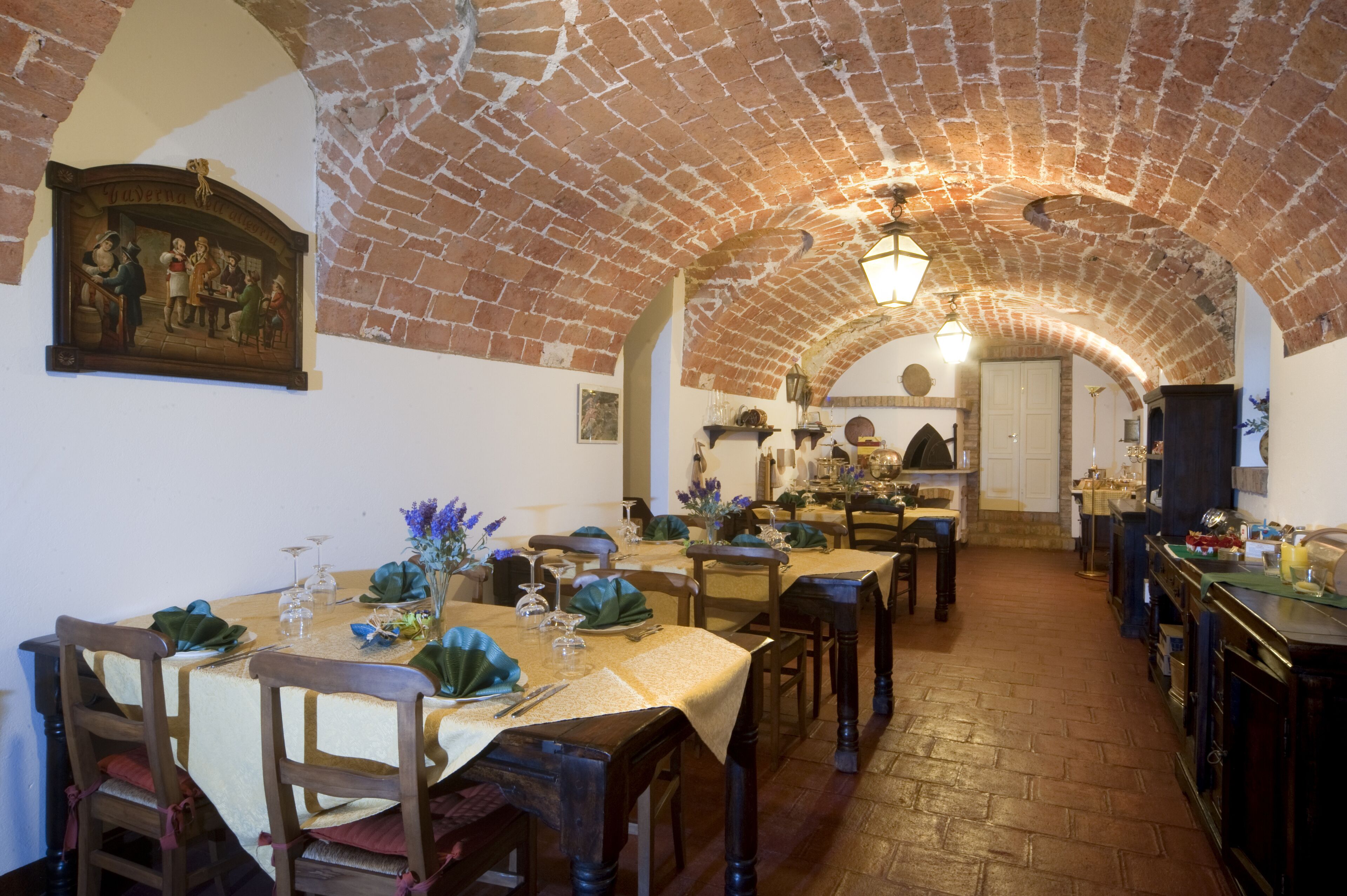 Un comedor con arcos de ladrillo, mesas y sillas de madera, y un cuadro en la pared.