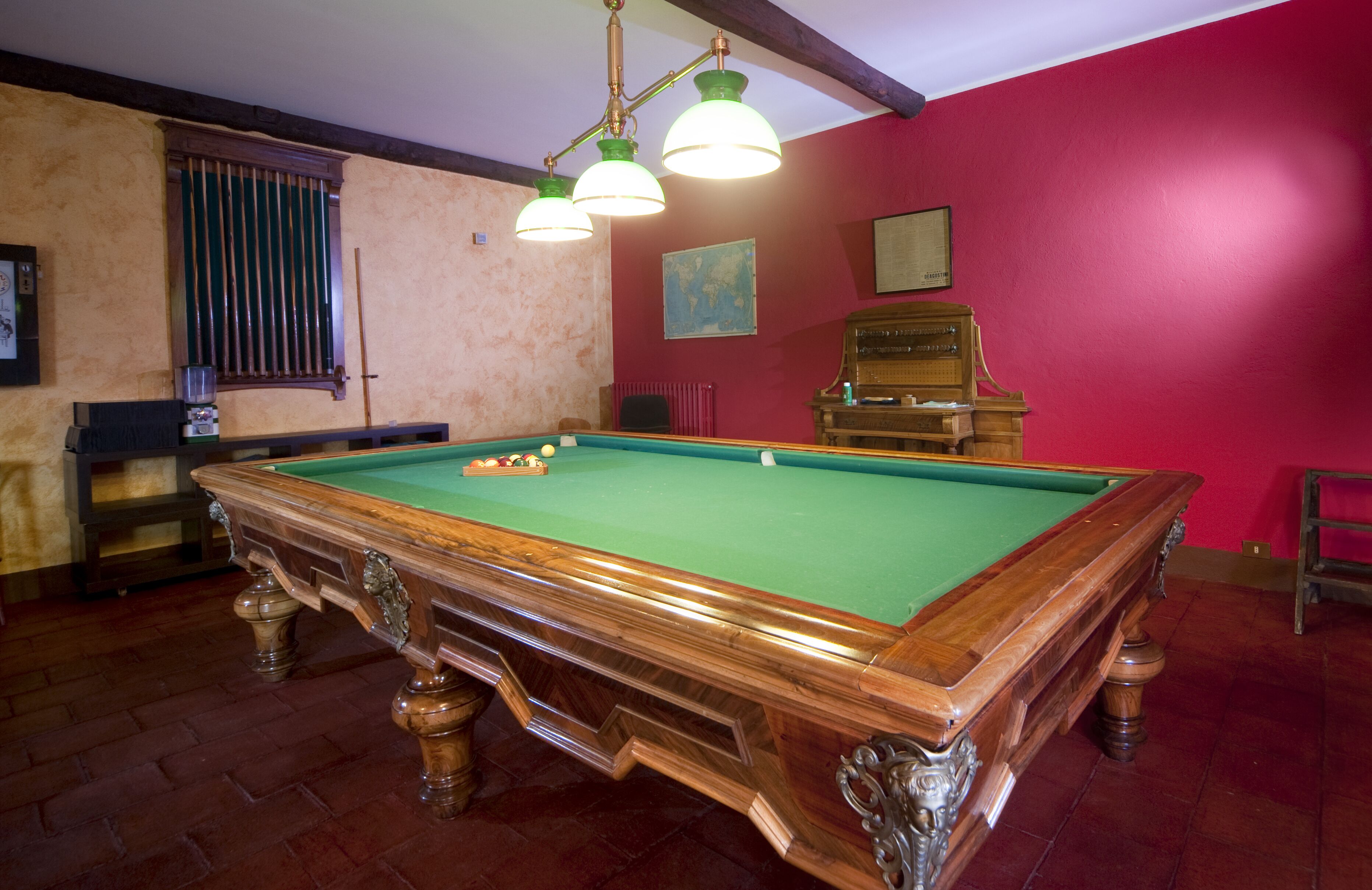 Una mesa de billar con superficie de fieltro verde, rodeada de muebles de madera y una pared roja.