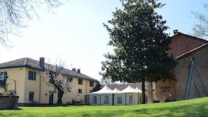 A courtyard with a grassy lawn, a yellow building, and a large tree. - tenuta la violina (Asti)