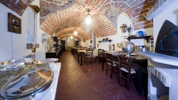 A traditional brick-walled dining area with tables and chairs, a long counter with a stove, and various kitchen utensils. - tenuta la violina (Asti)