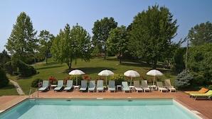 A swimming pool with lounge chairs and umbrellas, surrounded by trees and a grassy area. - tenuta la violina (Asti)
