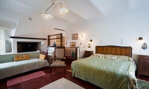 A bedroom with a bed, a chair, a sofa, a fireplace, and wall-mounted lights. - tenuta la violina (Asti)