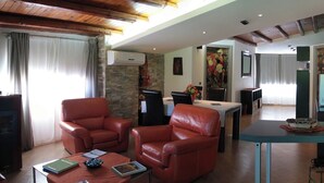 A living room with leather sofas, a coffee table with books, a TV, and a dining area with a table and chairs.