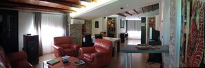 A living room with leather sofas, a coffee table with books, a TV, and a dining area with a table and chairs. - Camagna Country House Suite Guttuso (Partanna)