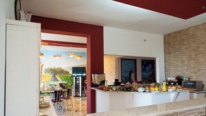 A modern kitchen with a marble countertop, a dining area with a table and chairs, and a view of a garden through an open door.