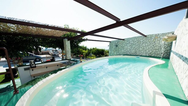 A swimming pool with a stone wall and a pergola structure.