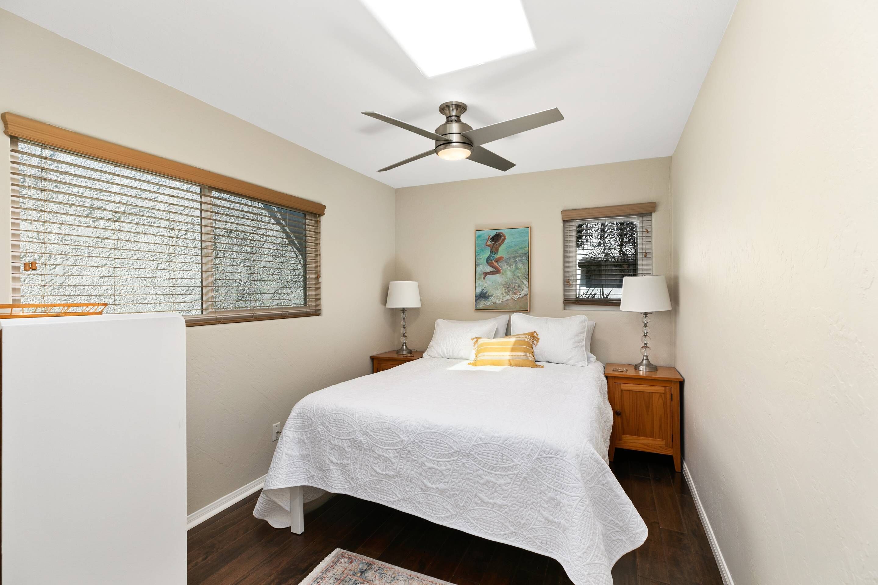 A bedroom with a bed, two nightstands, two lamps, a ceiling fan, and a window with blinds.