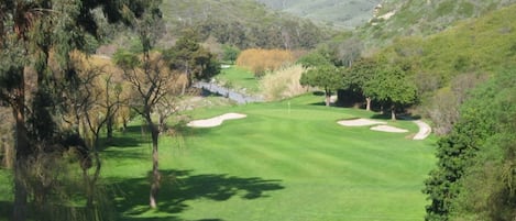 Un parcours de golf avec des bunkers de sable, des arbres et un paysage vallonné en arrière-plan.