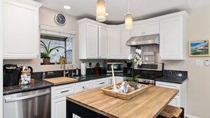 Une cuisine moderne avec des meubles blancs, un îlot central en bois, des appareils en acier inoxydable et des luminaires suspendus.