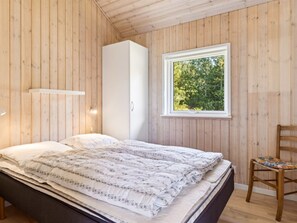 Een slaapkamer met een bed, een kledingkast, een raam met uitzicht op bomen, en een stoel.