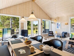 Een modern interieur met een houten plafond, grote ramen en een eethoek met zwarte lederen stoelen en een tafel gedekt met een theepot, kopjes en een schaal fruit.