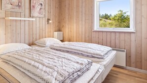 Een kamer met houten lambrisering, twee bedden, een raam met uitzicht op groen, en twee kunstwerken in lijsten aan de wand.