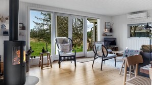 Un salon chaleureux avec un poêle à bois, des sièges confortables et de grandes fenêtres donnant sur l’extérieur.