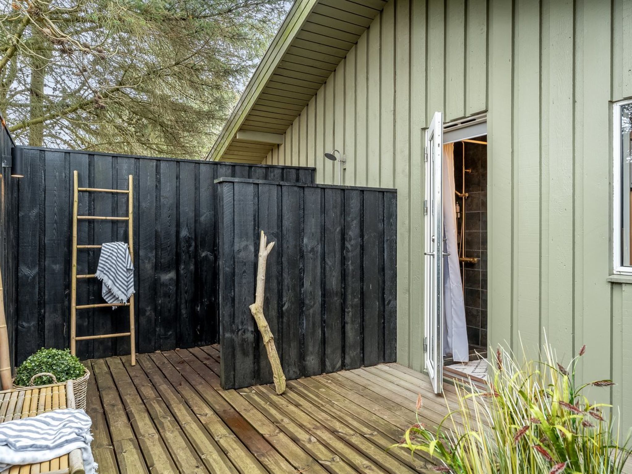 Una terraza de madera con cercado negro, una escalera y una puerta que da a un espacio cubierto.