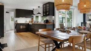 Une cuisine moderne avec des meubles de couleur sombre, une table à manger en bois, des chaises en osier et une grande fenêtre.