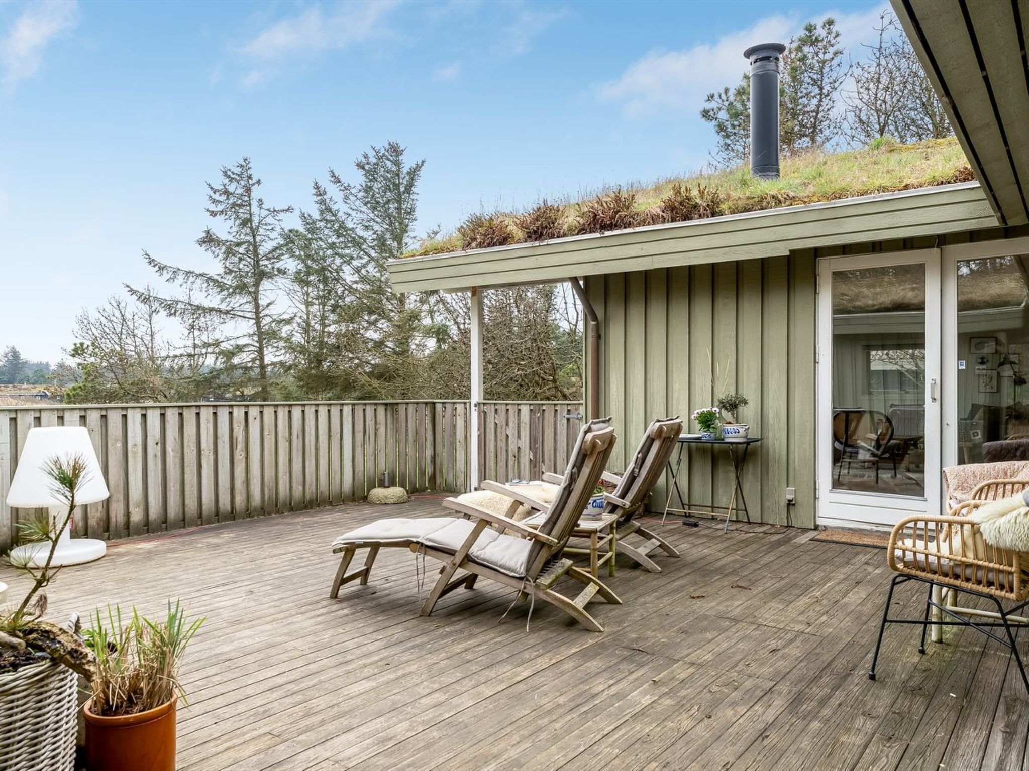 Une terrasse en bois avec des chaises longues, une petite table et une plante en pot.