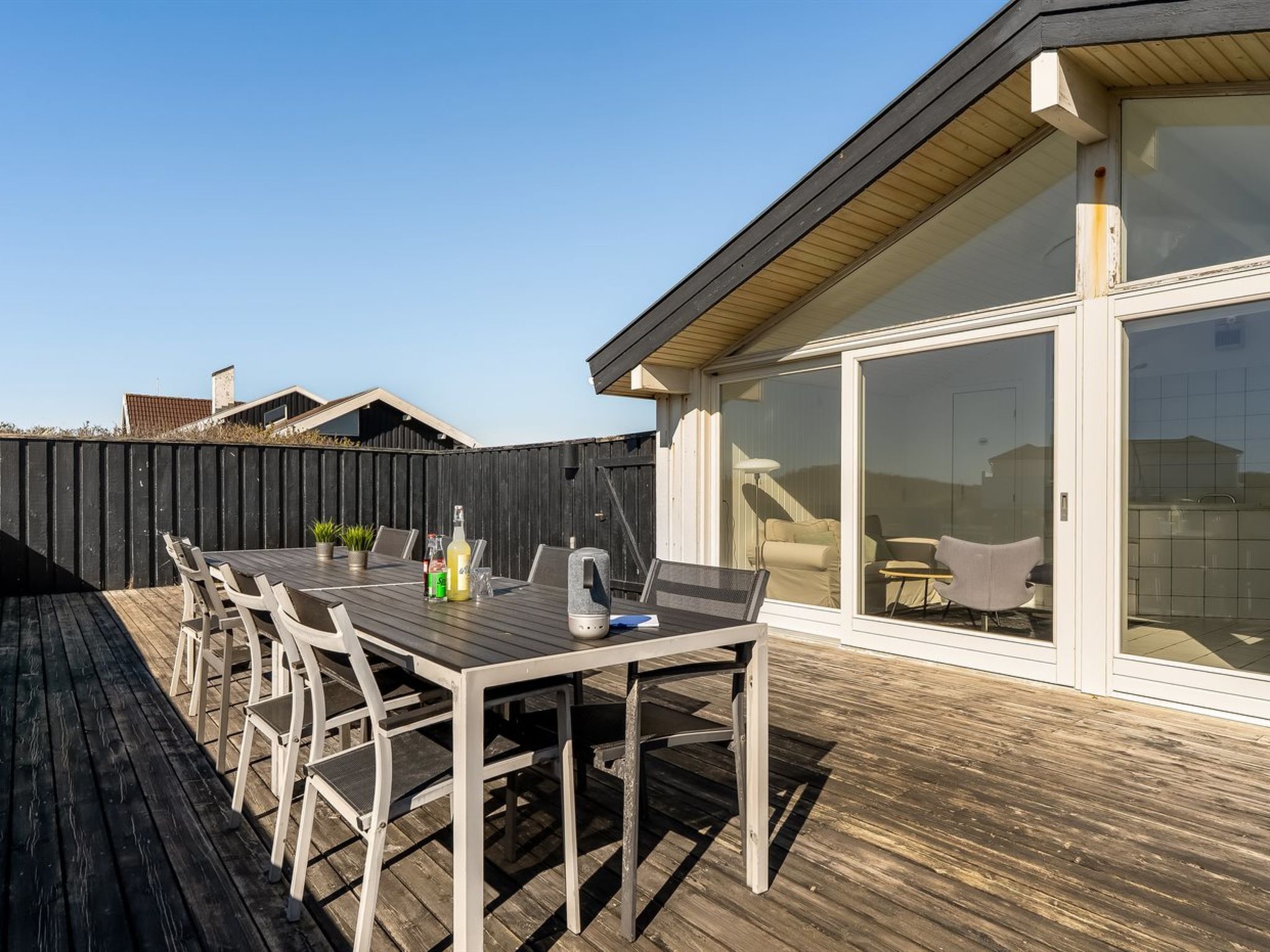A deck with a table and chairs, a sliding glass door leading to a patio area, and a wooden fence in the background.