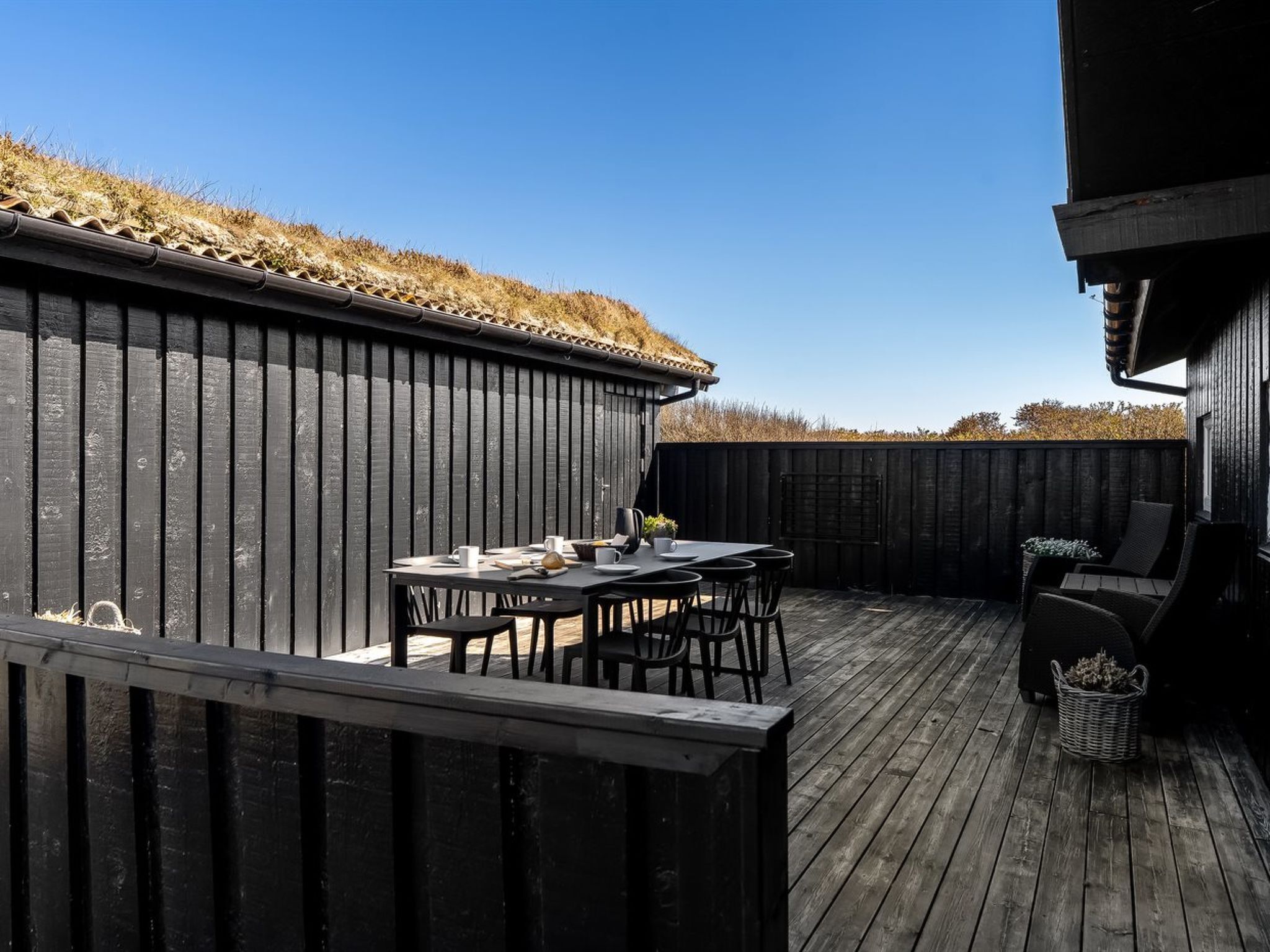 Eine Holzterrasse mit Tisch, Stühlen, einem Grill und einem schwarzen Zaun.