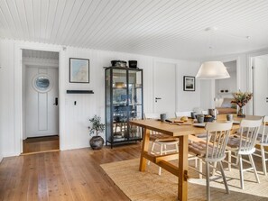 A dining area with a wooden table, white chairs, a rug, and a glass cabinet with dishes.
