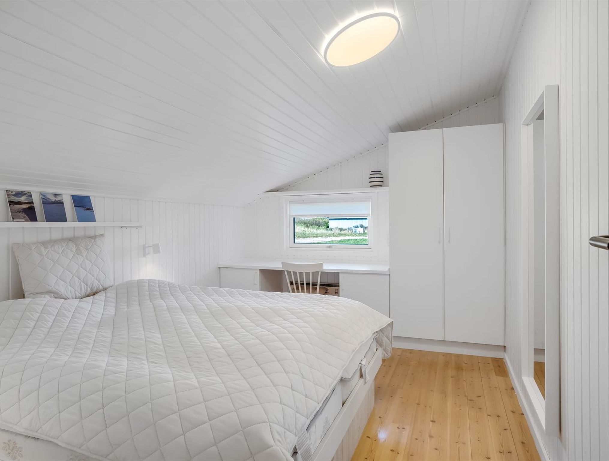 A bedroom with a bed, a desk, and a window.