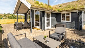 A modern house with a sloped roof, large windows, and a patio area with outdoor furniture.