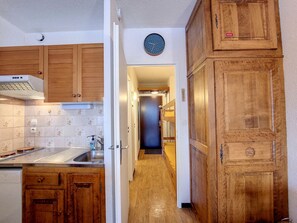 A narrow kitchen with wooden cabinets and a tiled backsplash. - Functional studio near slopes and shops, balcony and mountain corner (Montvalezan-La Rosière)