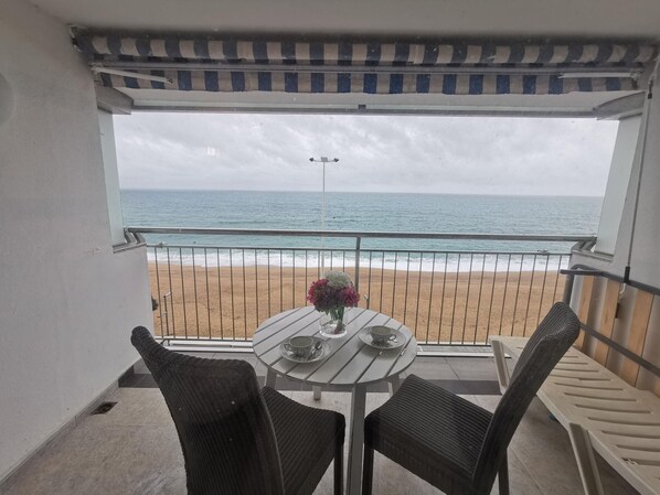 Un balcón con mesa y sillas, con vistas a una playa y el océano.