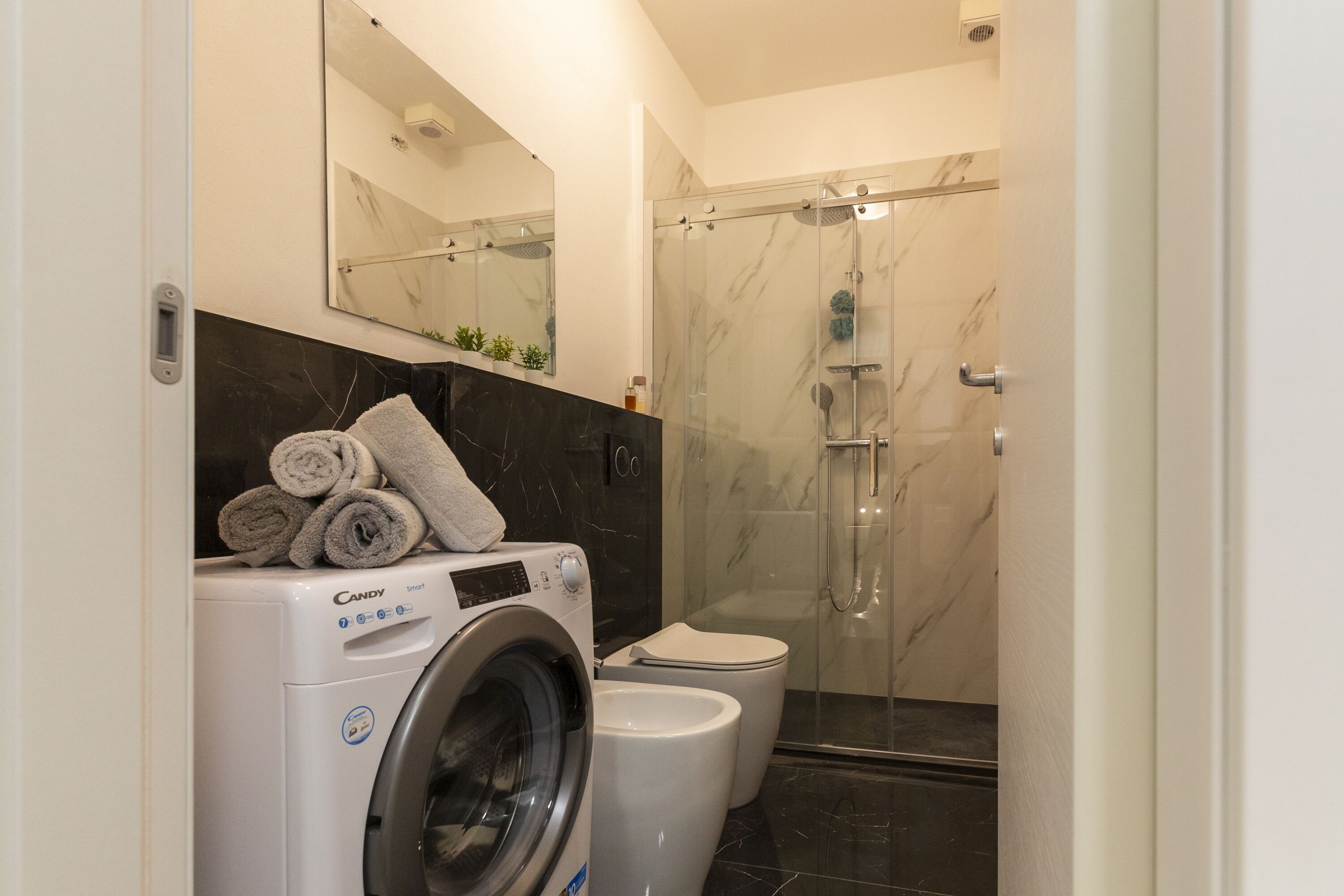 A modern bathroom with a washing machine, a toilet, and a glass-enclosed shower.