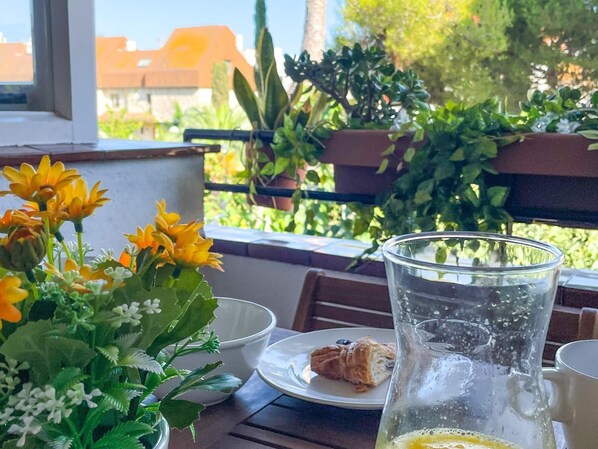 A table with a glass pitcher, a plate with a croissant, a bowl, and a potted plant with yellow flowers.