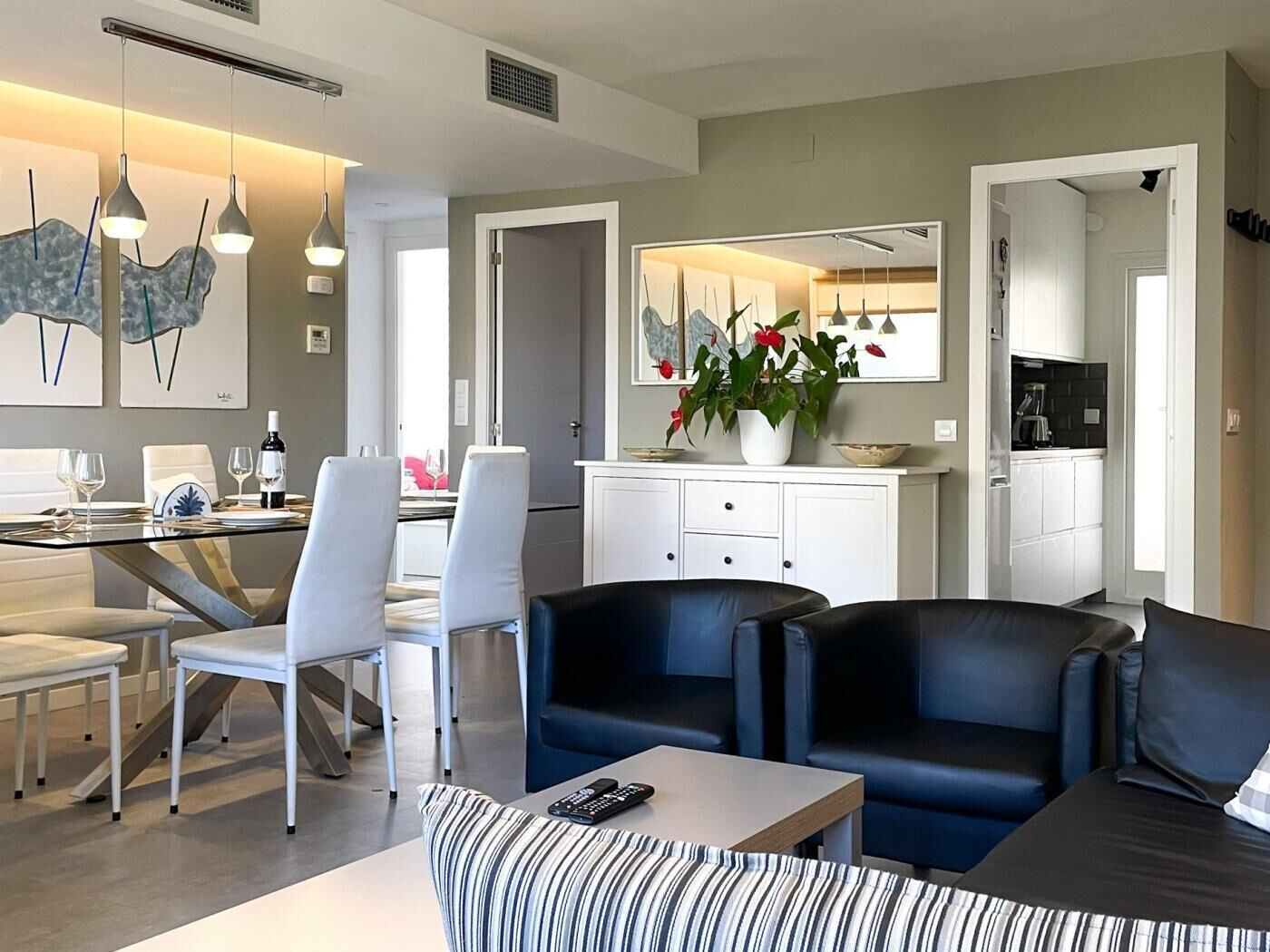 Een moderne woonkamer met een eethoek, een keuken op de achtergrond en een grote spiegel boven de eettafel.