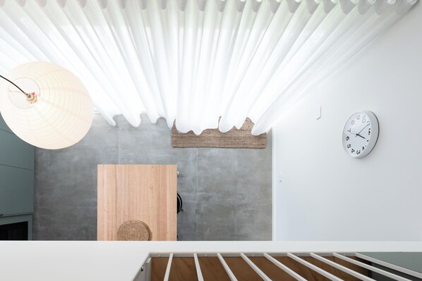 A modern interior with a concrete wall, a wooden door, a woven basket, a hanging light fixture, and a wall clock.