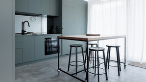 A modern kitchen with grey cabinets, a wooden countertop, and three black stools.