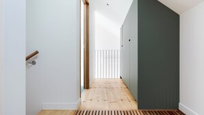 A narrow hallway with wooden flooring, white walls, and a dark green door.