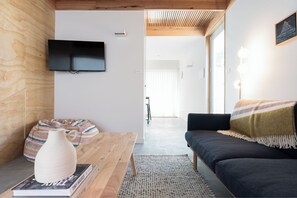 A modern living room with a wooden coffee table, a white vase, a striped bean bag, a dark sofa, and a television mounted on the wall.