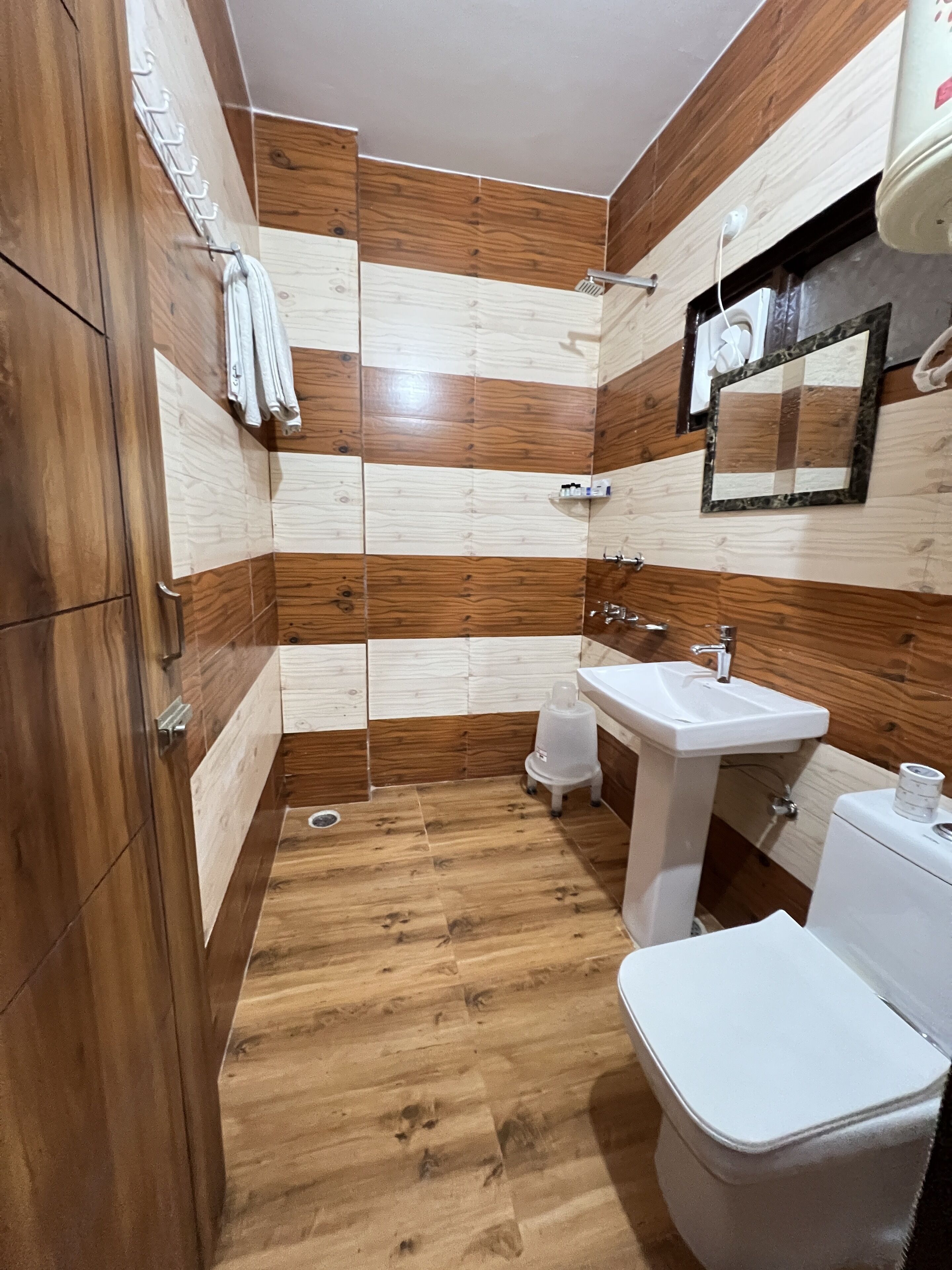 A bathroom with wooden panel walls, a white sink, a toilet, and a shower area.