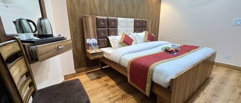 A hotel room with a wooden bed, a nightstand with a kettle, a chair, and a mirror.