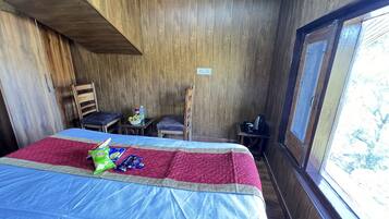 A wooden room with a bed, two chairs, a small table, and a window.